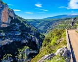 Vue panoramique des gorges de la Nesque, une route sinueuse longeant des falaises abruptes et une végétation luxuriante. Parfait pour une randonnée mémorable.