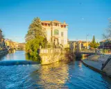 L'eau vive de la Sorgue traverse L'Isle-sur-la-Sorgue, bordée de maisons et d'un bâtiment blanc imposant.