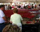 Des gens préparent une immense tarte aux fraises pour la fête de la fraise. Des fraises fraîches et des morceaux de pain sont disposés sur une grande table.