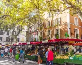 Ambiance animée au marché de Manosque, sous les platanes aux feuilles d'automne. Étals colorés de fruits et légumes frais, passants flânant.