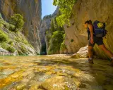 Randonneuse explorant la gorge du Toulourenc, traversant une rivière aux eaux cristallines bordée de falaises imposantes et de végétation luxuriante.