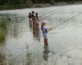 Des enfants pêchent dans le lac du Bartras, guidés par un adulte. L'eau reflète le ciel et la végétation.