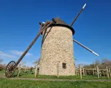 Le moulin de Maryline, une tour de pierre imposante sous un ciel bleu, se dresse fièrement avec ses ailes en bois.