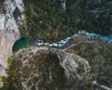 Vue aérienne de la Fontaine de Vaucluse, avec son bassin émeraude et la rivière Sorgue serpentant à travers une gorge boisée.