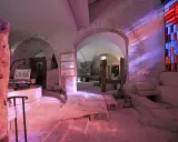 Intérieur d'un musée du verre et du vitrail, avec des arches en pierre, des outils anciens et un vitrail coloré projetant des rayons lumineux.