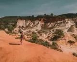 Une femme au chapeau admire le paysage spectaculaire de la carrière d'ocre du Vaucluse, avec ses falaises colorées et sa végétation luxuriante.