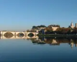 Le pont d'Avignon se reflète dans le Rhône, avec le Palais des Papes et l'île de la Barthelasse en arrière-plan.