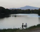Deux pêcheurs sur un bateau profitent du calme du plan d'eau du Revestidou, avec des montagnes en arrière-plan.