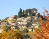 Village de Joucas, France, en automne. Les maisons en pierre s'étagent sur la colline, entourées d'arbres aux couleurs flamboyantes.