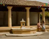 Deux femmes discutent près d'une fontaine sous un auvent orné de fanions colorés, ambiance de marché à Rochefort-du-Gard.