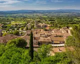 Vue aérienne du village de Bonnieux, avec ses toits de tuiles ocres, son église et la campagne environnante verdoyante. Le marché de Bonnieux est un lieu animé.
