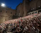 Foule nombreuse assise sur des gradins, devant un palais, pour la Fête de la Musique à Avignon.