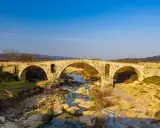 Le **pont Julien**, un ancien pont de pierre à trois arches, enjambe une rivière asséchée bordée de rochers et de végétation.