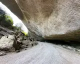 Le chemin menant au fort de Buoux serpente sous un immense surplomb rocheux, offrant un aperçu de la nature sauvage.