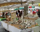 Ambiance animée au marché de Lourmarin, avec des étals de produits locaux, herbes aromatiques et bouteilles d'huile d'olive.