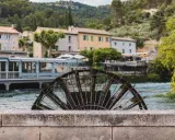 Roue à aubes rouillée sur la Sorgue, avec des maisons provençales en arrière-plan. Le **gouffre de Fontaine-de-Vaucluse** est une source d'eau d'une beauté saisissante.