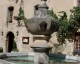 Fontaine en pierre avec des têtes de gargouilles à Venasque, Vaucluse. L'eau coule doucement dans le bassin, entouré de végétation luxuriante.