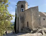 Le clocher de Notre-Dame d'Alidon, avec sa cloche visible, se dresse fièrement sous un ciel bleu. Des visiteurs admirent le paysage.