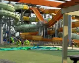 Des toboggans colorés et sinueux dominent le parc aquatique de Monteux. Des visiteurs se préparent à glisser, certains portant des bouées vertes.