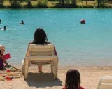Journée baignade à L'Isle-sur-la-Sorgue. Des enfants jouent dans l'eau turquoise, d'autres sur le sable. Une mère surveille, profitant du soleil.