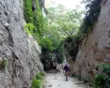Un randonneur explore les **gorges du Régalon**, un sentier rocailleux bordé de falaises abruptes et de végétation luxuriante.