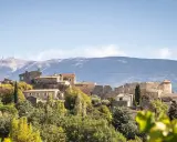 Vue d'un faucon village perché sur une colline, avec une église et des ruines médiévales. Le Mont Ventoux domine l'horizon.