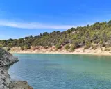 Le lac du Paty, aux eaux turquoise, est bordé de rochers et de collines verdoyantes sous un ciel bleu.
