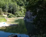 Des baigneurs profitent d'une rivière aux eaux claires près du rocher des abeilles, certains escaladent la paroi rocheuse.