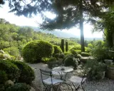 Le jardin de la louve, un havre de paix verdoyant avec une table et des chaises invitant à la détente, surplombe une vallée luxuriante.