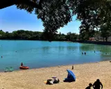 Baignade et détente sur la plage du lac de Bonnieux, sous le feuillage d'un grand arbre. L'eau turquoise invite à la baignade.