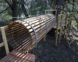 Un tunnel en bois et métal, partie d'un parcours aventure dans la forêt enchantée Venasque. Une échelle mène à une plateforme.