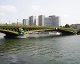 Le pont Mirabeau, avec ses statues de sirènes, enjambe la Seine, bordée par des immeubles modernes et des péniches.