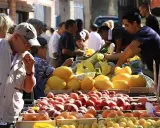 Ambiance animée au marché de Pernes-les-Fontaines. Des étals débordent de fruits colorés, pêches, melons, et agrumes. Des clients choisissent leurs produits.