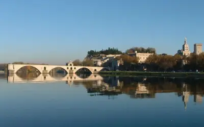 Le pont d'Avignon se reflète dans le Rhône, avec le Palais des Papes et l'île de la Barthelasse en arrière-plan.
