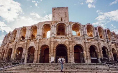 Visiter Arles : une personne tient un bébé sur les marches de l'amphithéâtre romain, sous un ciel bleu et nuageux.
