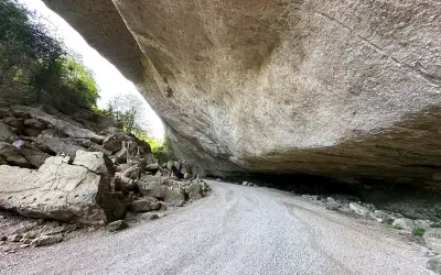 Le chemin menant au fort de Buoux serpente sous un immense surplomb rocheux, offrant un aperçu de la nature sauvage.