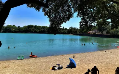 Baignade et détente sur la plage du lac de Bonnieux, sous le feuillage d'un grand arbre. L'eau turquoise invite à la baignade.