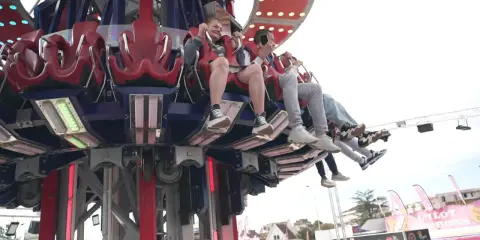 Des jeunes s'amusent dans une attraction de la fete foraine 84, leurs pieds balançant dans le vide.