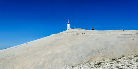 Le Mont Ventoux, sommet aride sous un ciel bleu intense, dominé par une tour de télécommunication.