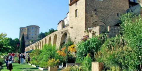 Jardin luxuriant devant le **château de Lauris**, avec ses murs de pierre et ses arches médiévales.