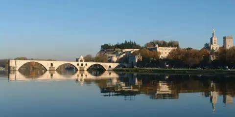 Le pont d'Avignon se reflète dans le Rhône, avec le Palais des Papes et l'île de la Barthelasse en arrière-plan.