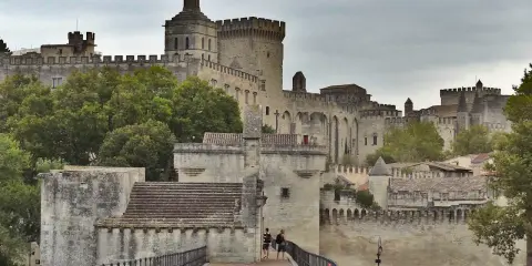 Le Palais des Papes, un incontournable pour tout guide Avignon, se dresse majestueusement. Des touristes explorent ce site historique.