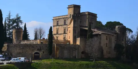 Le majestueux **Château de Lourmarin** se dresse sur une colline, ses pierres ocres baignées de soleil sous un ciel bleu. Des cyprès élancés l'entourent.