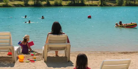 Journée baignade à L'Isle-sur-la-Sorgue. Des enfants jouent dans l'eau turquoise, d'autres sur le sable. Une mère surveille, profitant du soleil.
