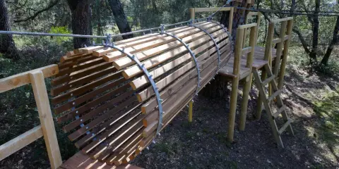 Un tunnel en bois et métal, partie d'un parcours aventure dans la forêt enchantée Venasque. Une échelle mène à une plateforme.