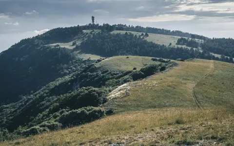 Vue panoramique du Moure Negre, avec une tour de télécommunication au sommet, des collines verdoyantes et un sentier sinueux.