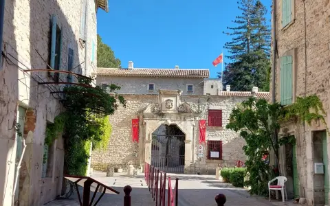 L'entrée majestueuse du **château de Thézan** s'ouvre sur une cour pavée, ornée de drapeaux rouges et d'une végétation luxuriante.