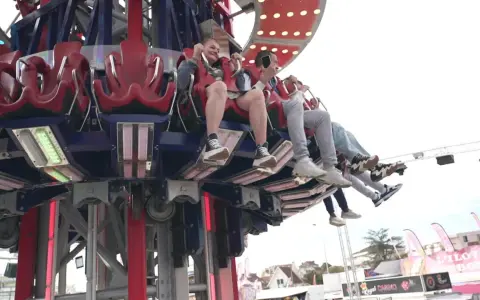 Des jeunes s'amusent dans une attraction de la fete foraine 84, leurs pieds balançant dans le vide.
