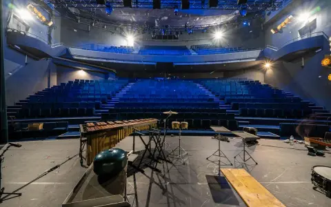 Scène de concert vide avec sièges bleus, marimba, batterie et projecteur, prête pour un spectacle à la Scala Provence.