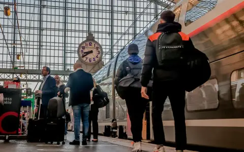 Voyageurs attendant le train pour Apt, sous une grande horloge dans une gare.